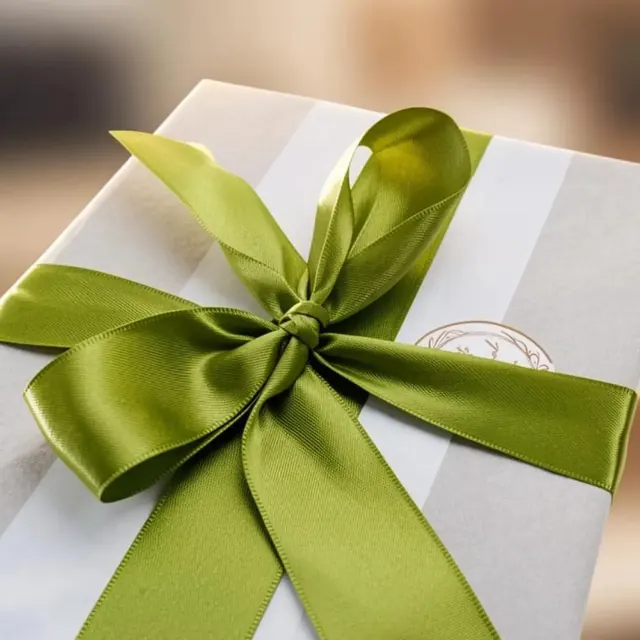 Álbum embrulhado para presente em papel branco, com laço de cetim verde e o selo da marca
