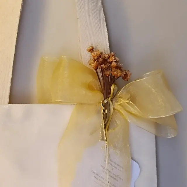 Sacola de tecido da Dinda Criativa com laço de organza dourado e flores secas, pronta para entrega